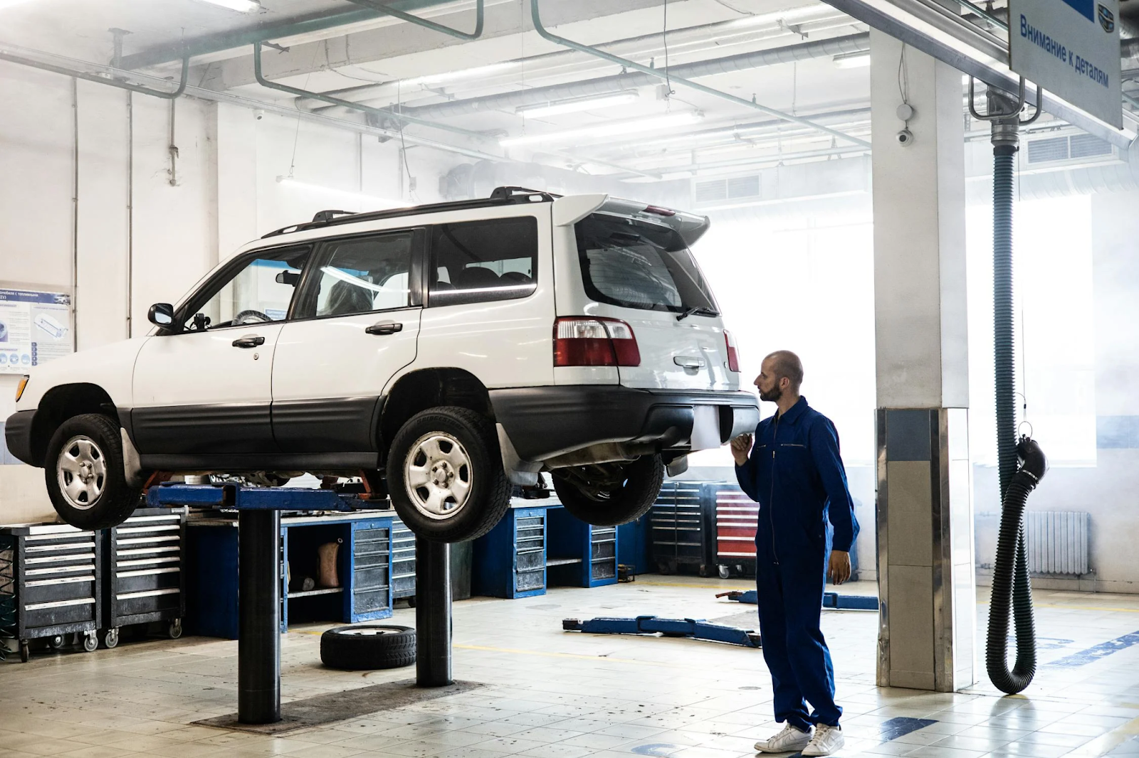 A mechanic lifts a car using a hydraulic jack in a garage setting, showcasing vehicle maintenance work.